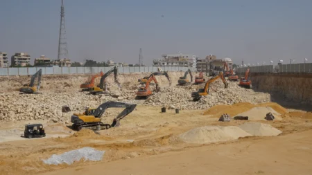 Excavators working the excavation floor at BeauRivage Plaza, Mokattam skyline beyond the hoarding